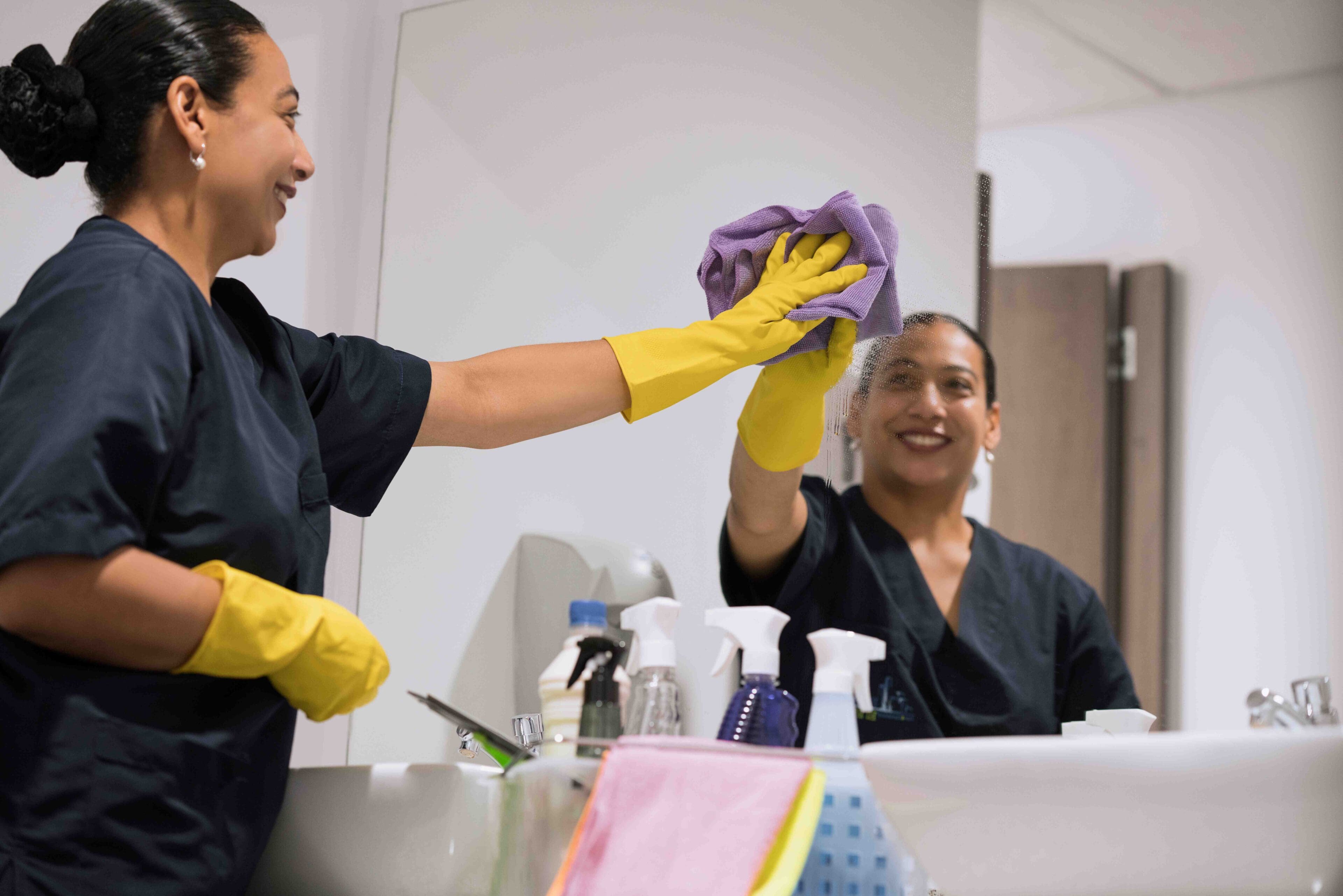 A woman in yellow gloves is holding a purple cloth.