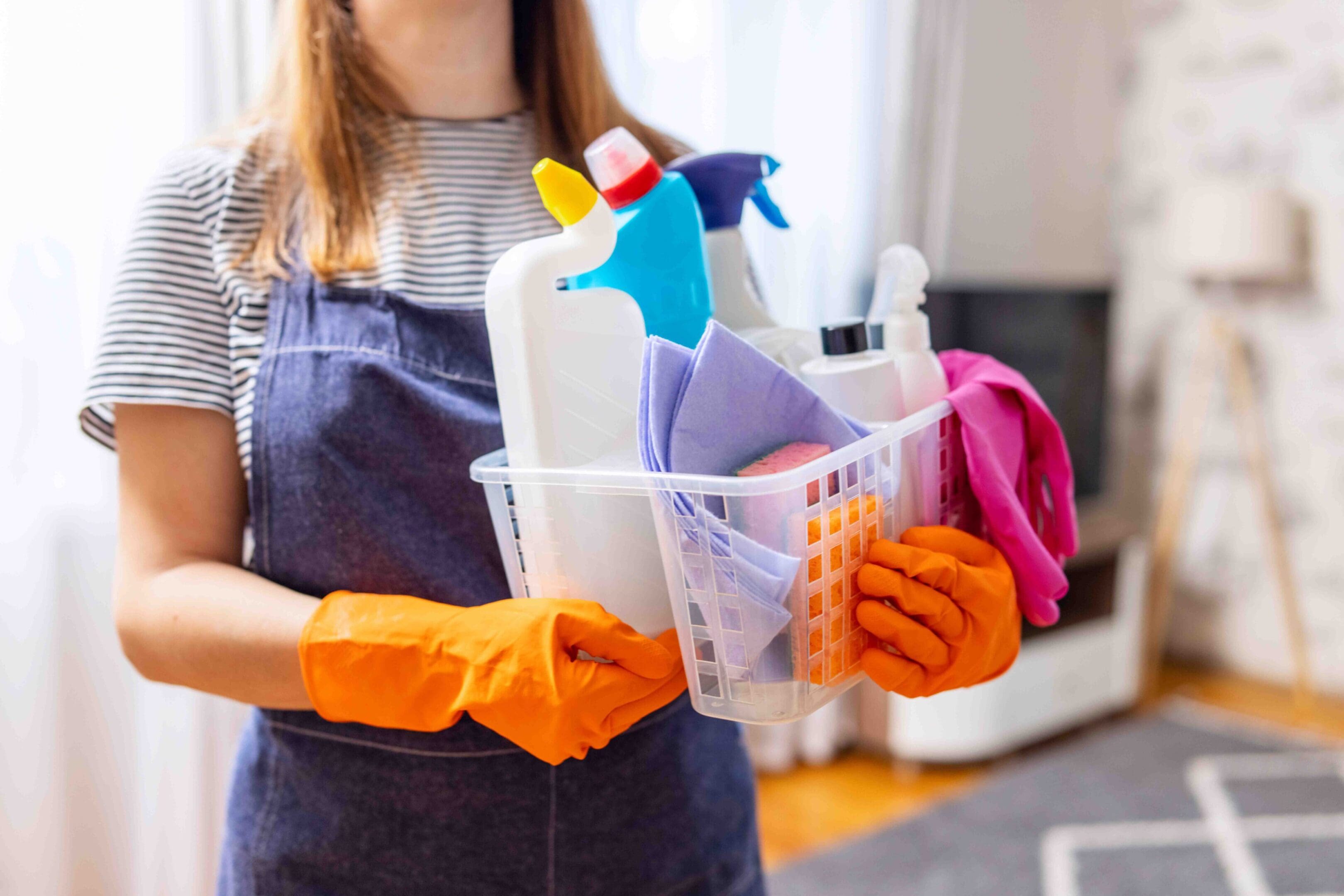 Woman in rubber gloves with basket of cleaning supplies ready to clean up her apartment. Housewife has many household chores, domestic work and professional cleaning service. Low depth of field